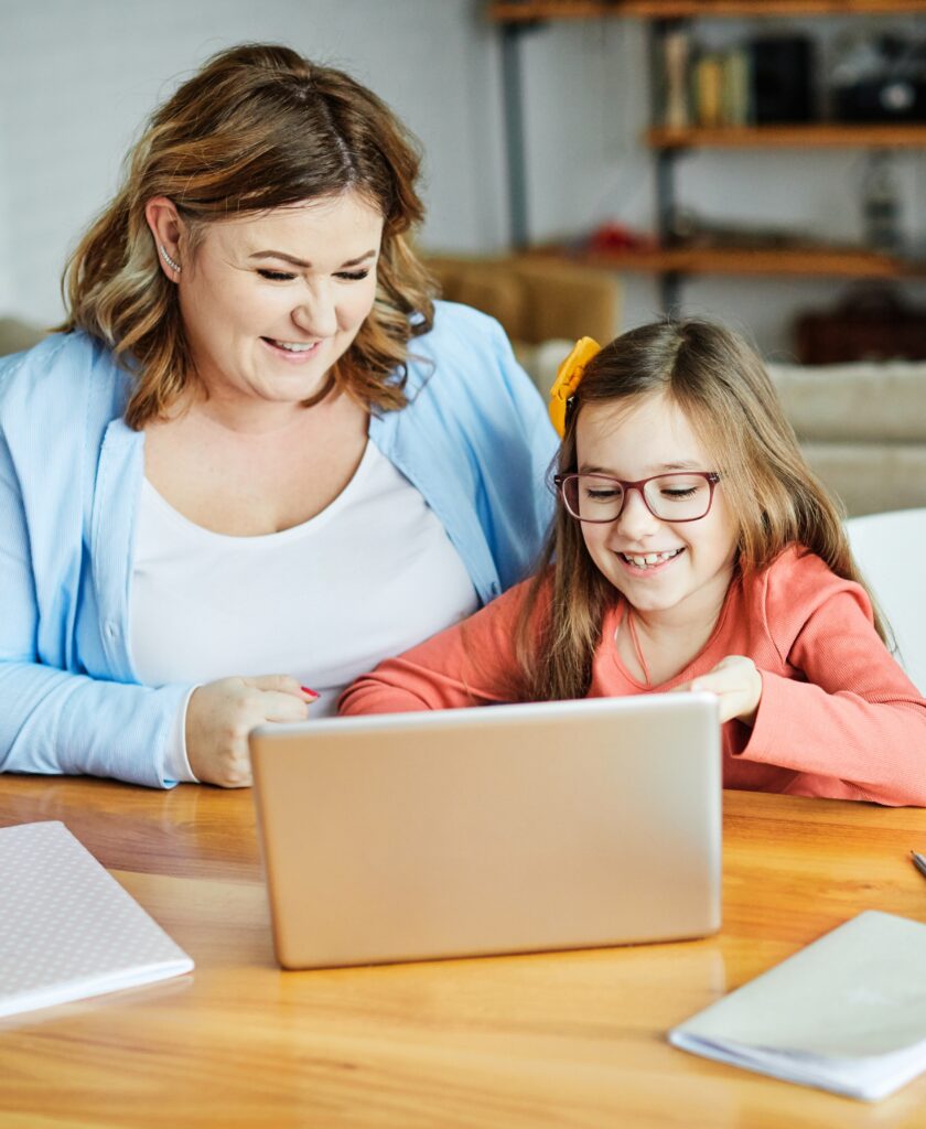 A parent and child at a table, looking at a laptop together