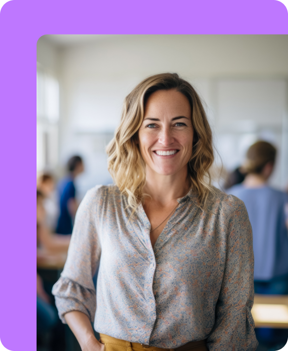Smiling woman standing in a classroom or school setting with students blurred in the background.