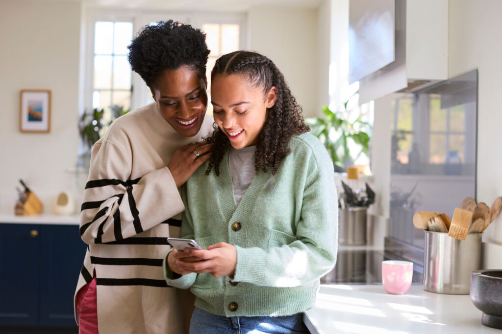 mother talking with teenage daughter at home and looking at mobile phone together