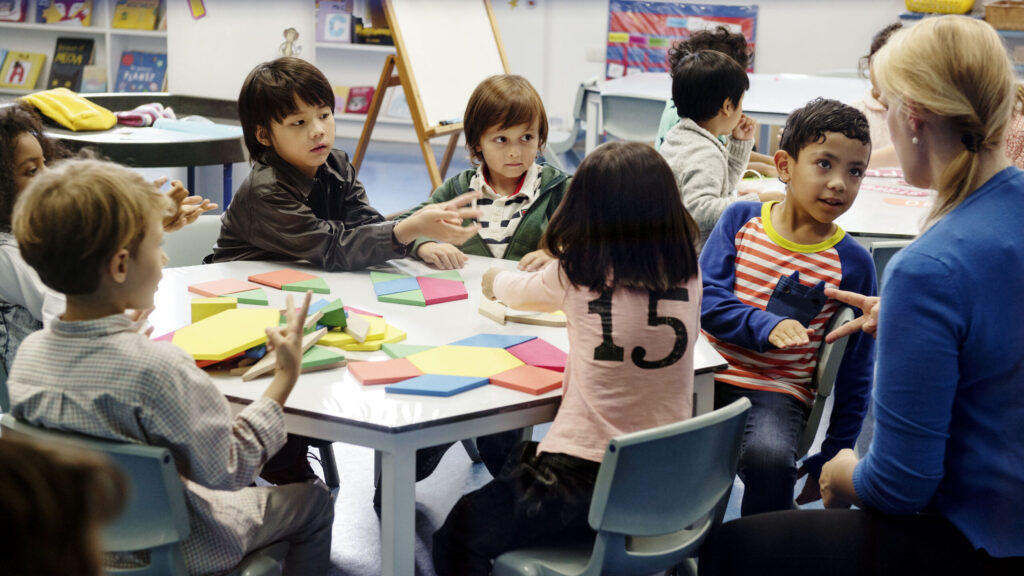 elementary school students playing with blocks around classroom table
