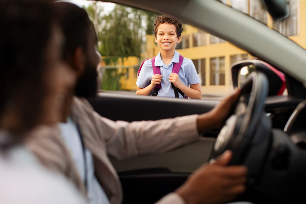 Mother and father dropping off son coming to school in the morning, schoolboy smiling to parents, view from inside car